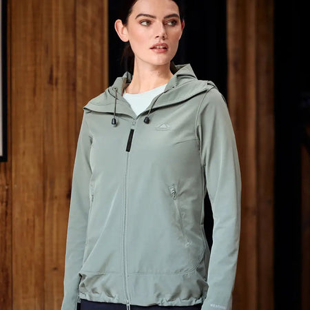 Woman wearing a green jacket with a hood indoors against a wooden background