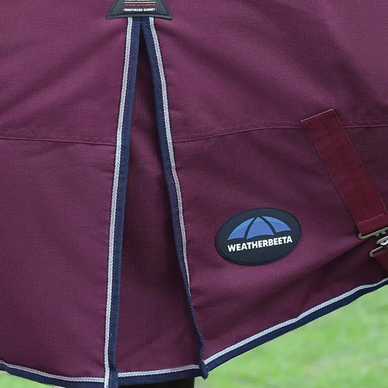 Close-up of a purple Weatherbeeta horse blanket with branding on a grass background