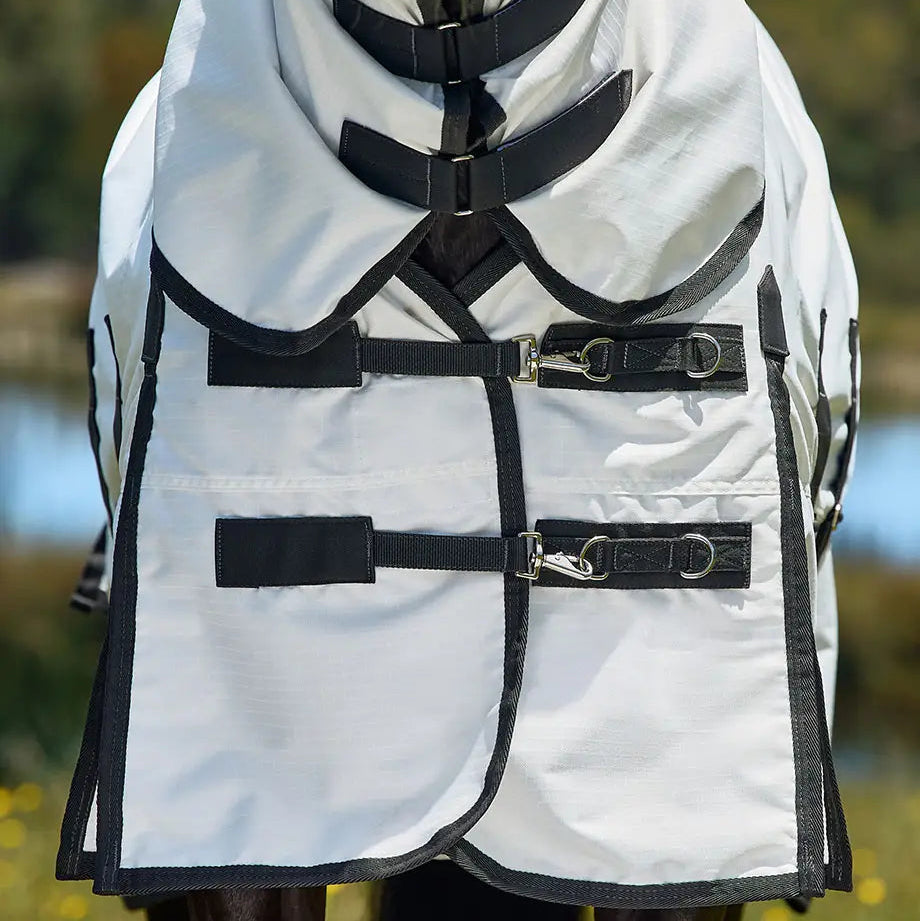 Horse wearing a white raincoat with black straps in a grassy field.