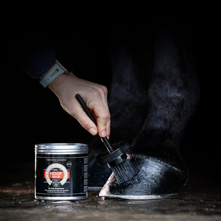 Person applying a black substance from a can to a shoe using a brush on a dark background.