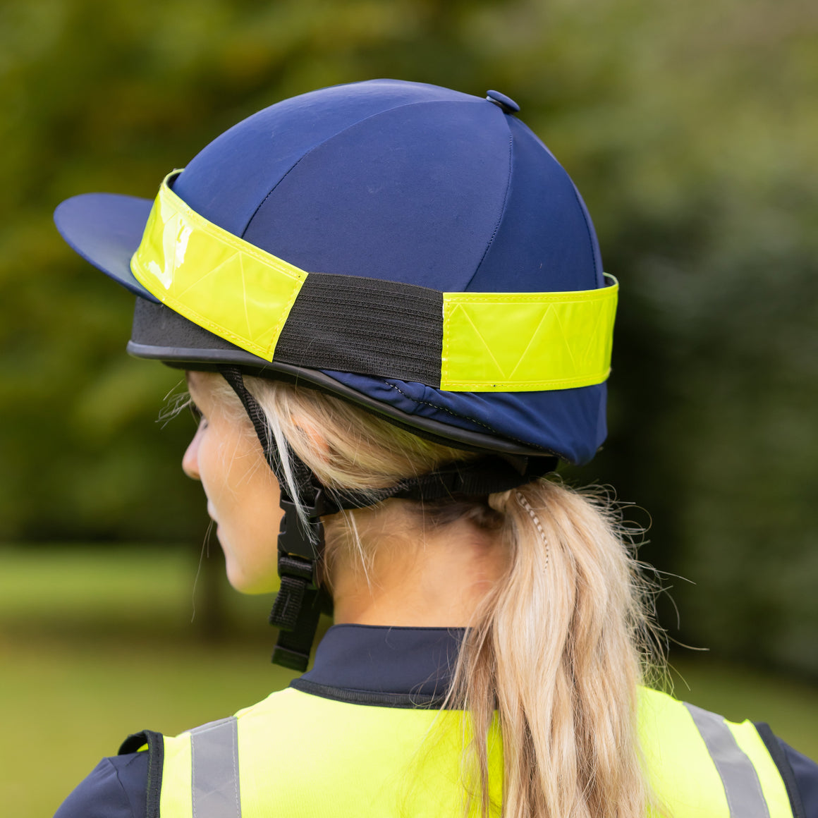 Person wearing a blue helmet with a yellow reflective band and a high-visibility vest outdoors.