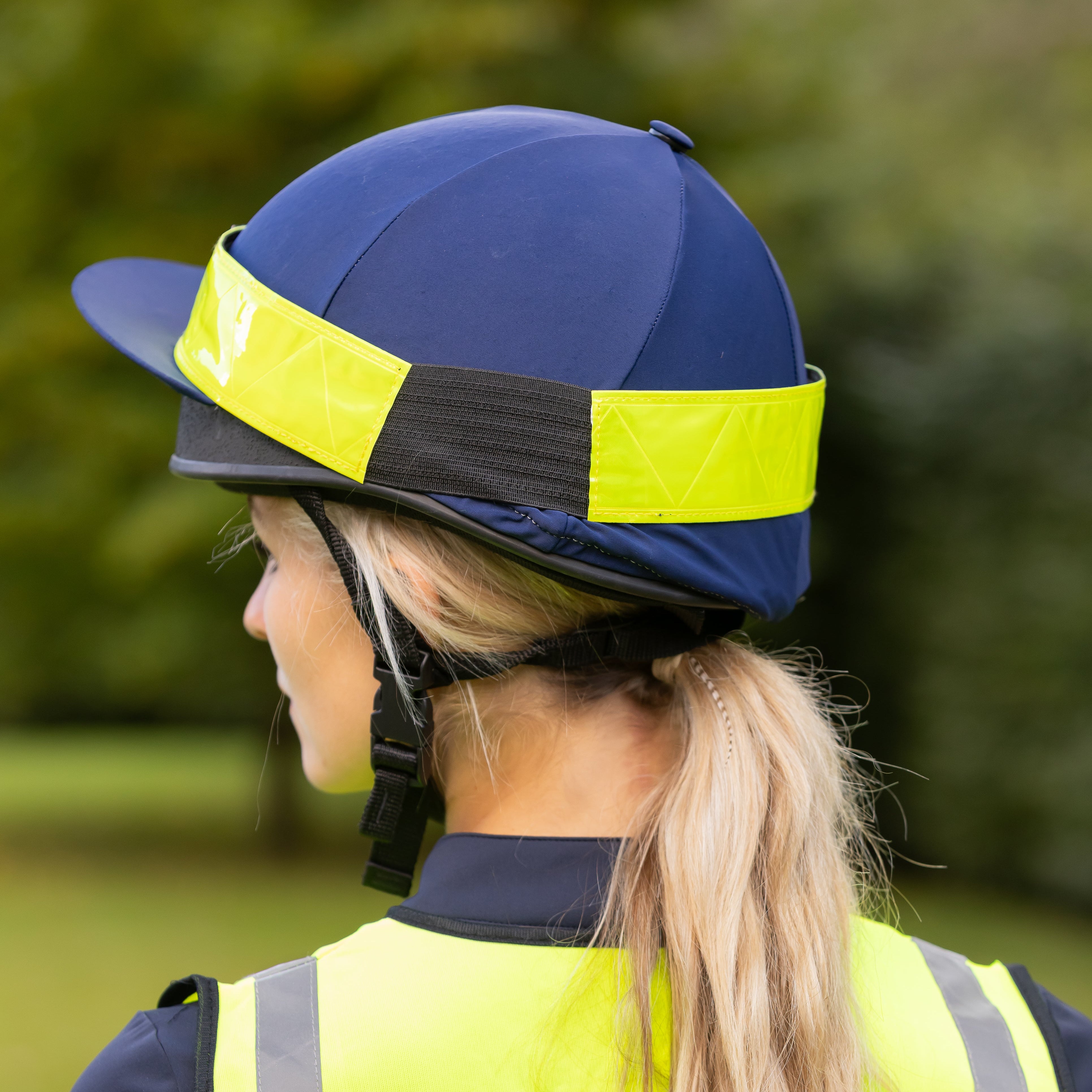 Person wearing a blue helmet with a yellow reflective band and a high-visibility vest outdoors.