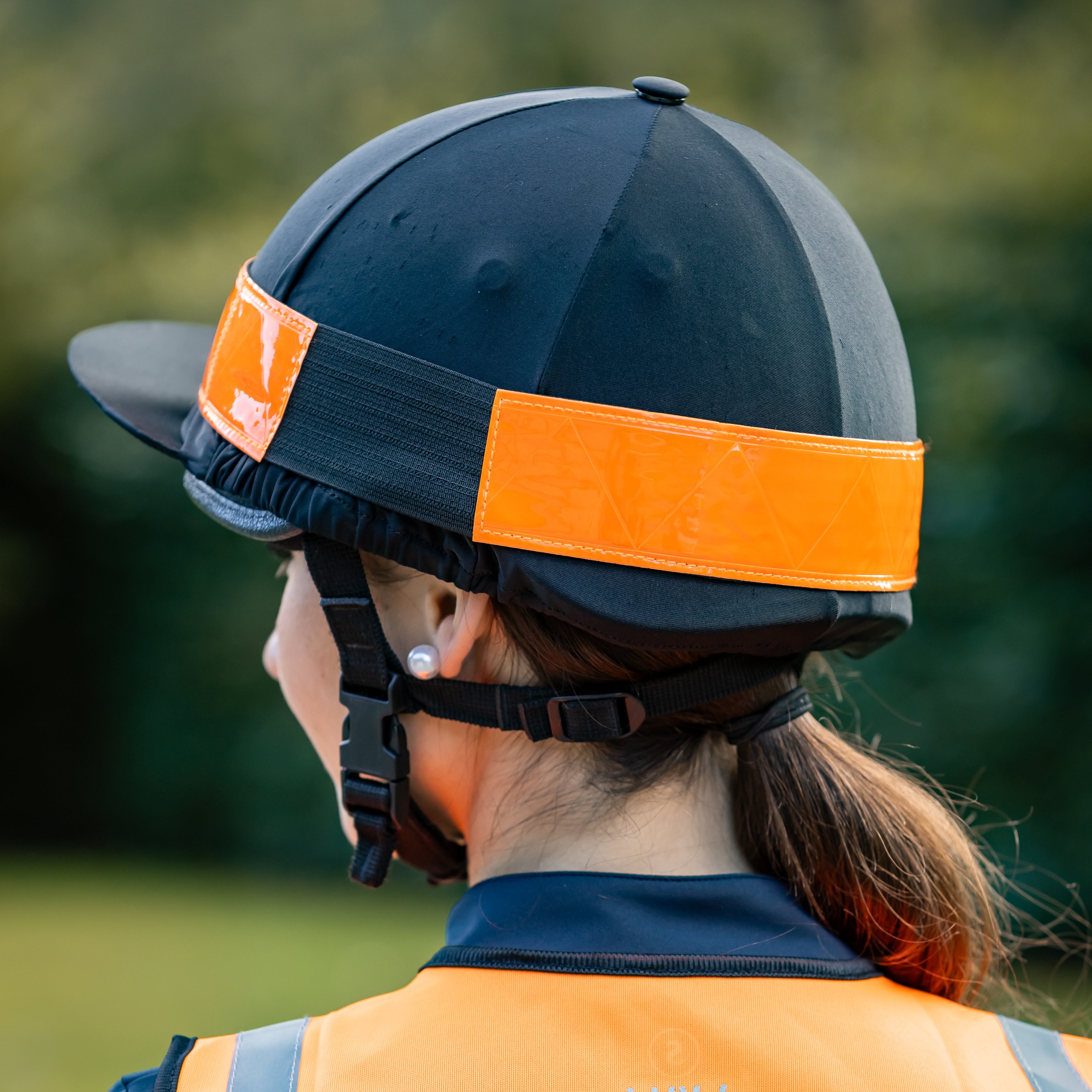 Person wearing a navy helmet with orange straps and an orange and navy vest with a logo.