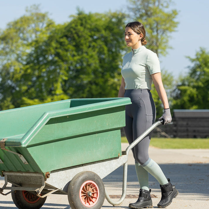 Person pushing a green wheelbarrow outdoors on a sunny day