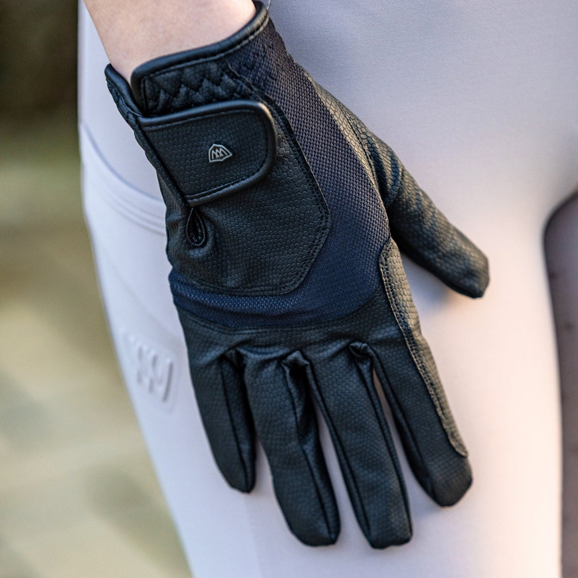 Black equestrian glove on a rider's hand with a blurred background