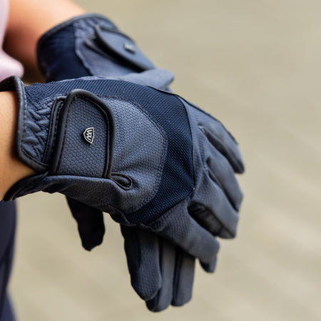Navy blue gloves held in a person's hand against a neutral background