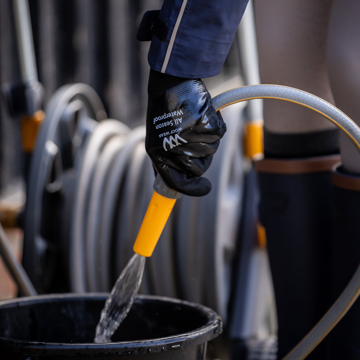 Person wearing a black glove with text, holding a yellow tool over a black bucket.
