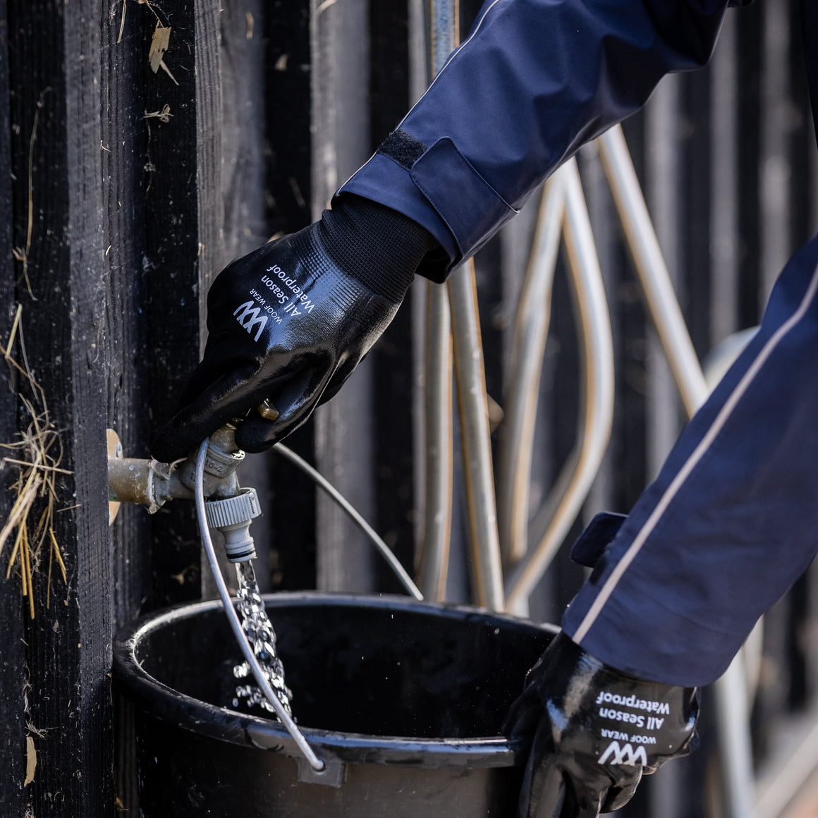 Person wearing gloves and interacting with a black bucket and hose in an industrial setting