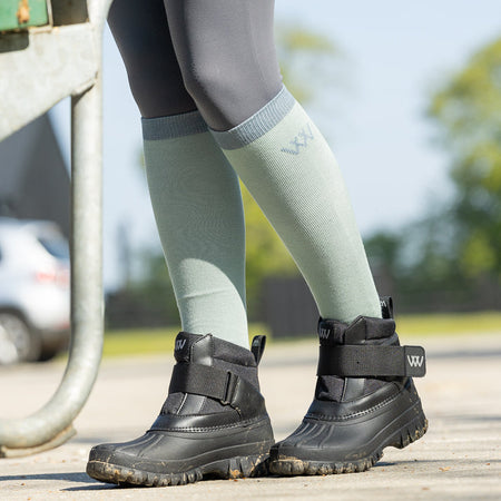 Person wearing black boots and green knee-high socks on a blurred outdoor background