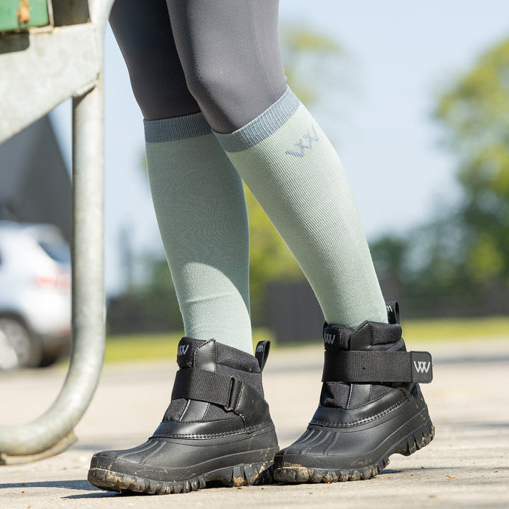 Person wearing black boots and green knee-high socks on a blurred outdoor background